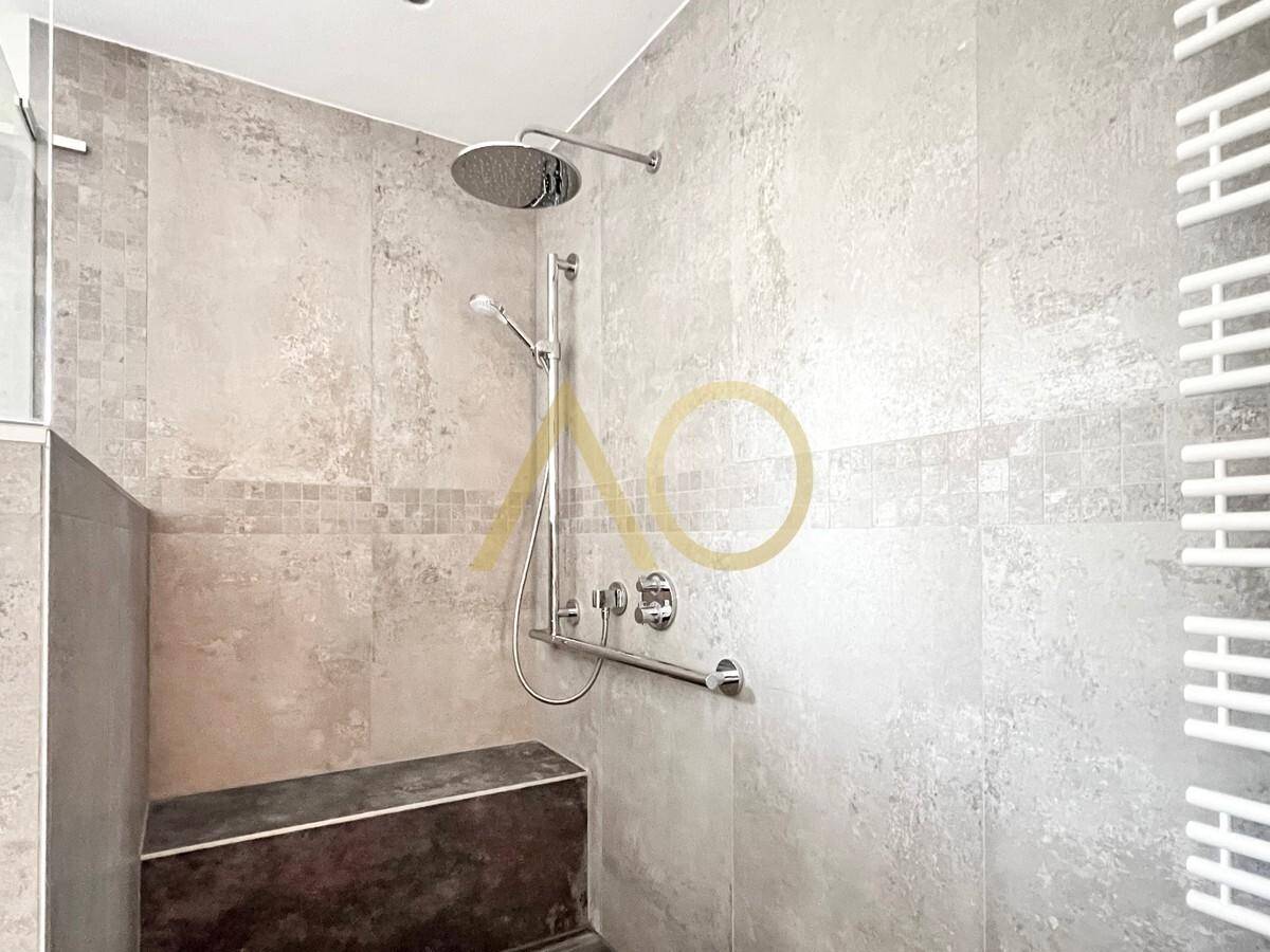 Detailansicht der modernen begehbaren Dusche mit Regenduschkopf und Haltegriff.