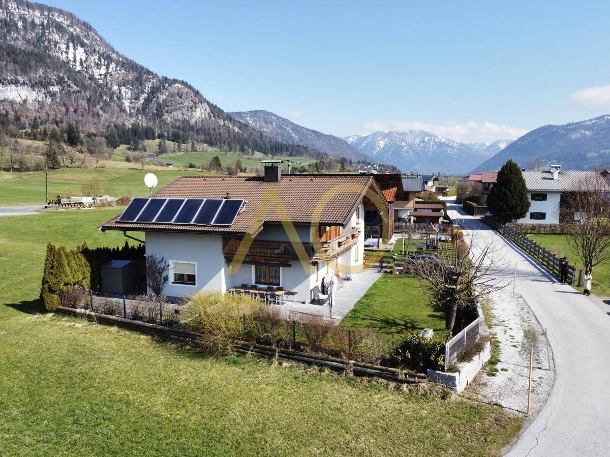 Haus mit Solaranlage auf dem Dach, umgeben von grüner Landschaft und Bergen.