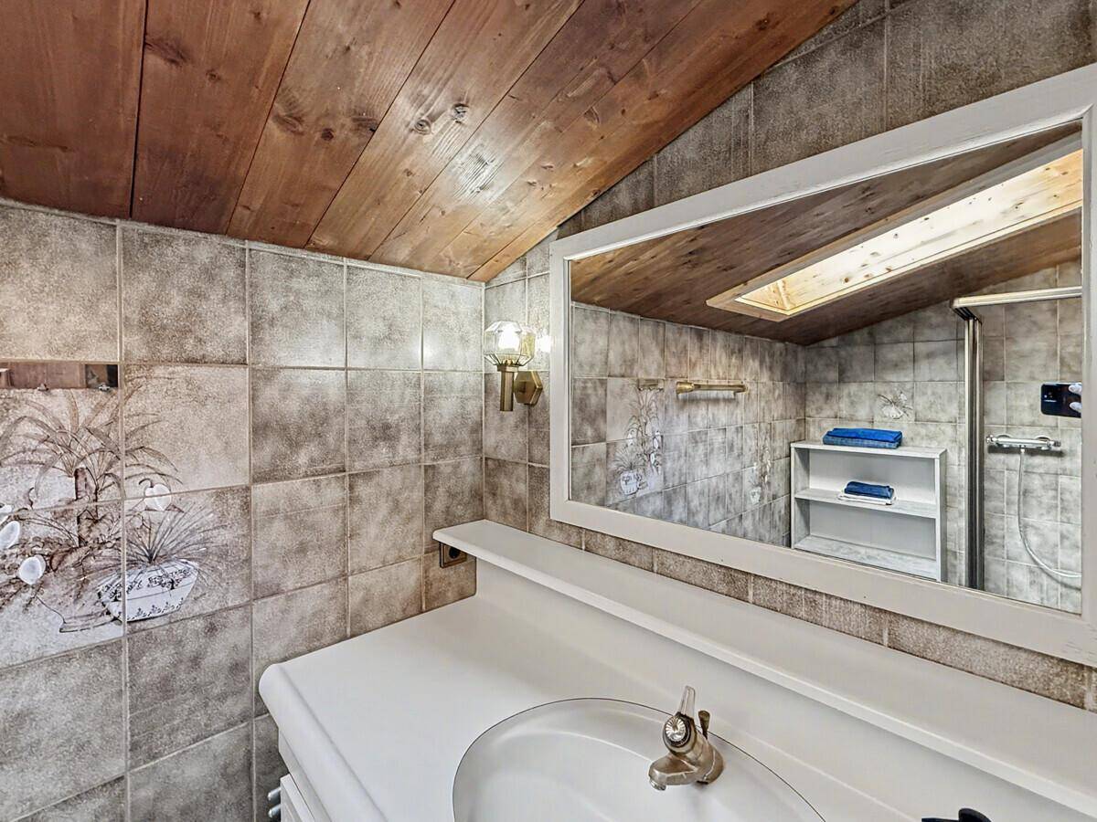 Badezimmer mit Waschbecken, Spiegel und rustikaler Holzdecke, durch Dachfenster erhellt.