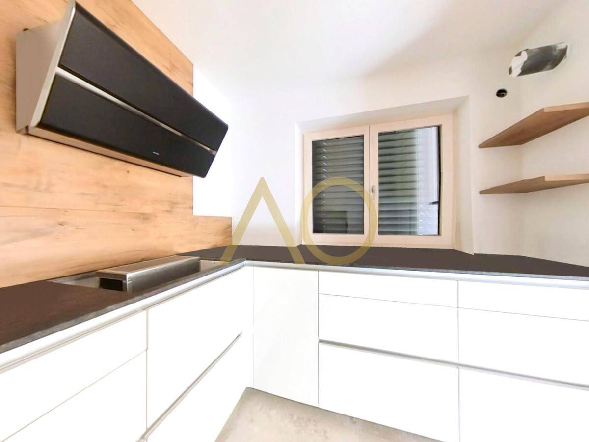 Moderne Küche mit weißen Schränken, dunkler Arbeitsplatte und Holzakzenten an der Wand.