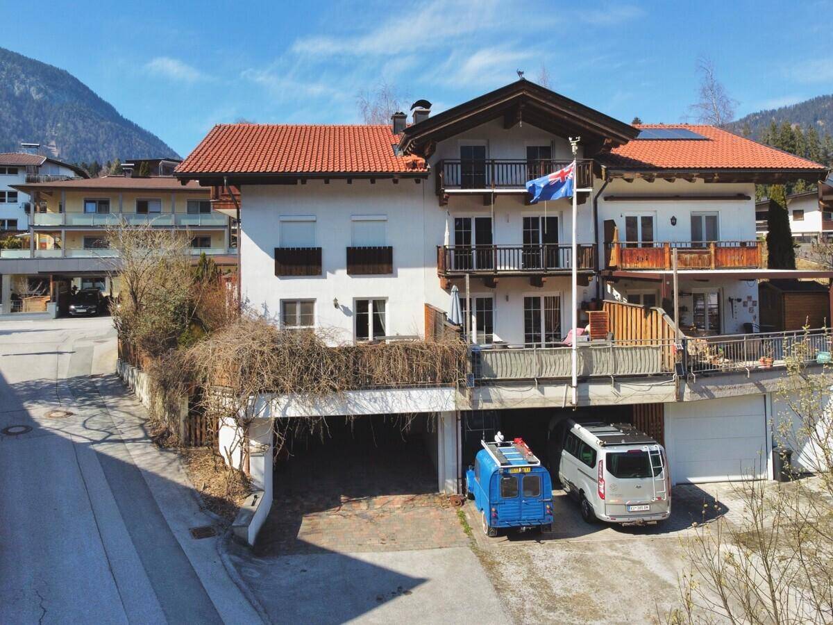 Mehrfamilienhaus mit mehreren Balkonen, Garagen und Bergblick in ländlicher Umgebung.