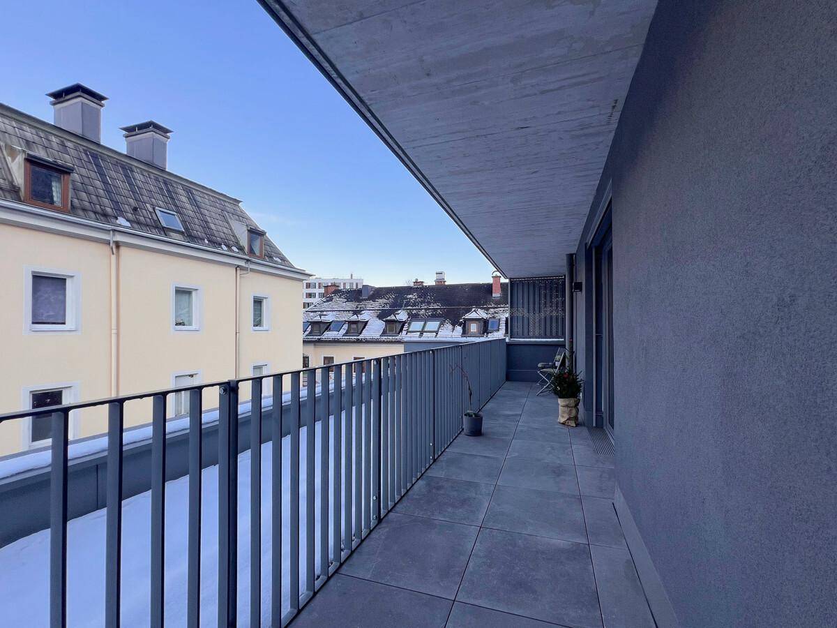 Balkon mit Fliesenboden und Blick auf die Dächer der Nachbargebäude.