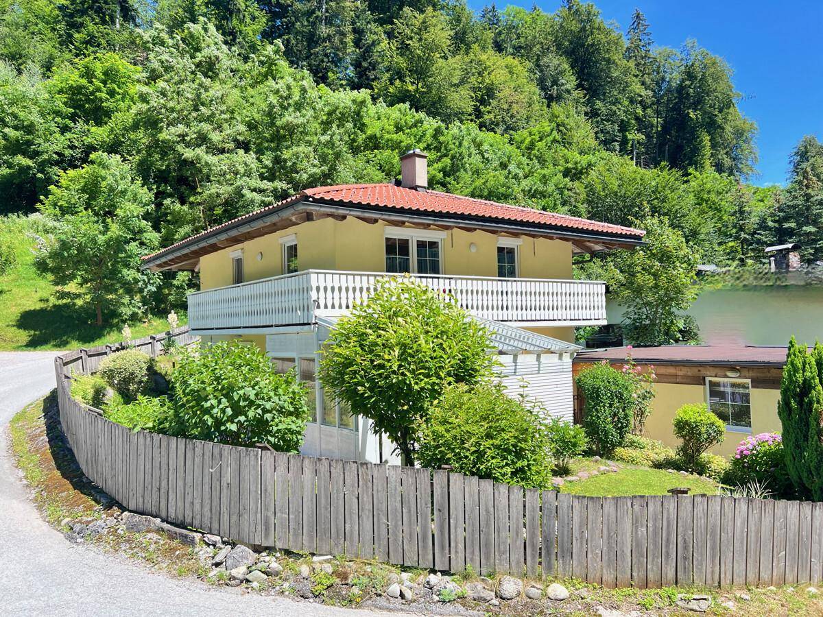 Charmantes Haus mit gelber Fassade, rotem Dach und Balkon, umgeben von üppiger grüner Natur.