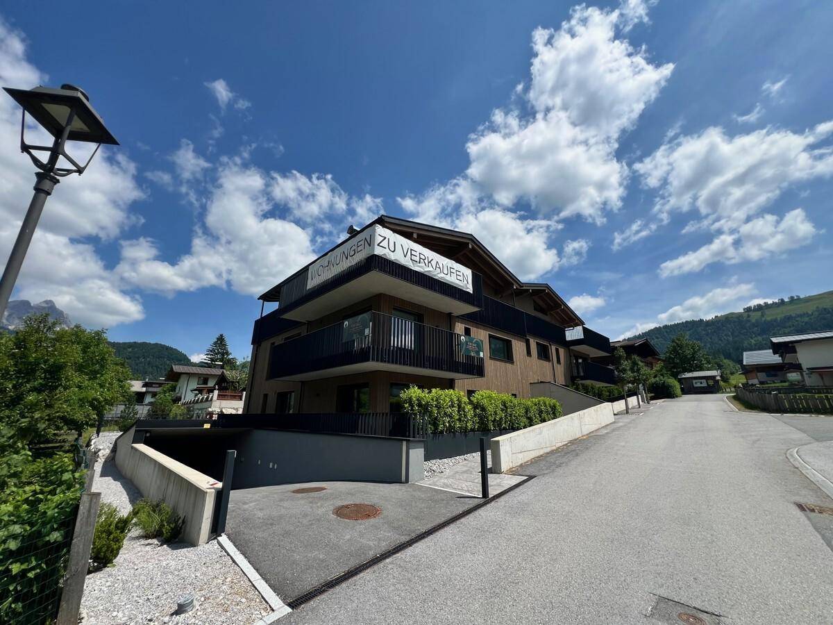 Modernes Wohngebäude mit Holzverkleidung und Balkonen unter blauem Himmel an einem sonnigen Tag.