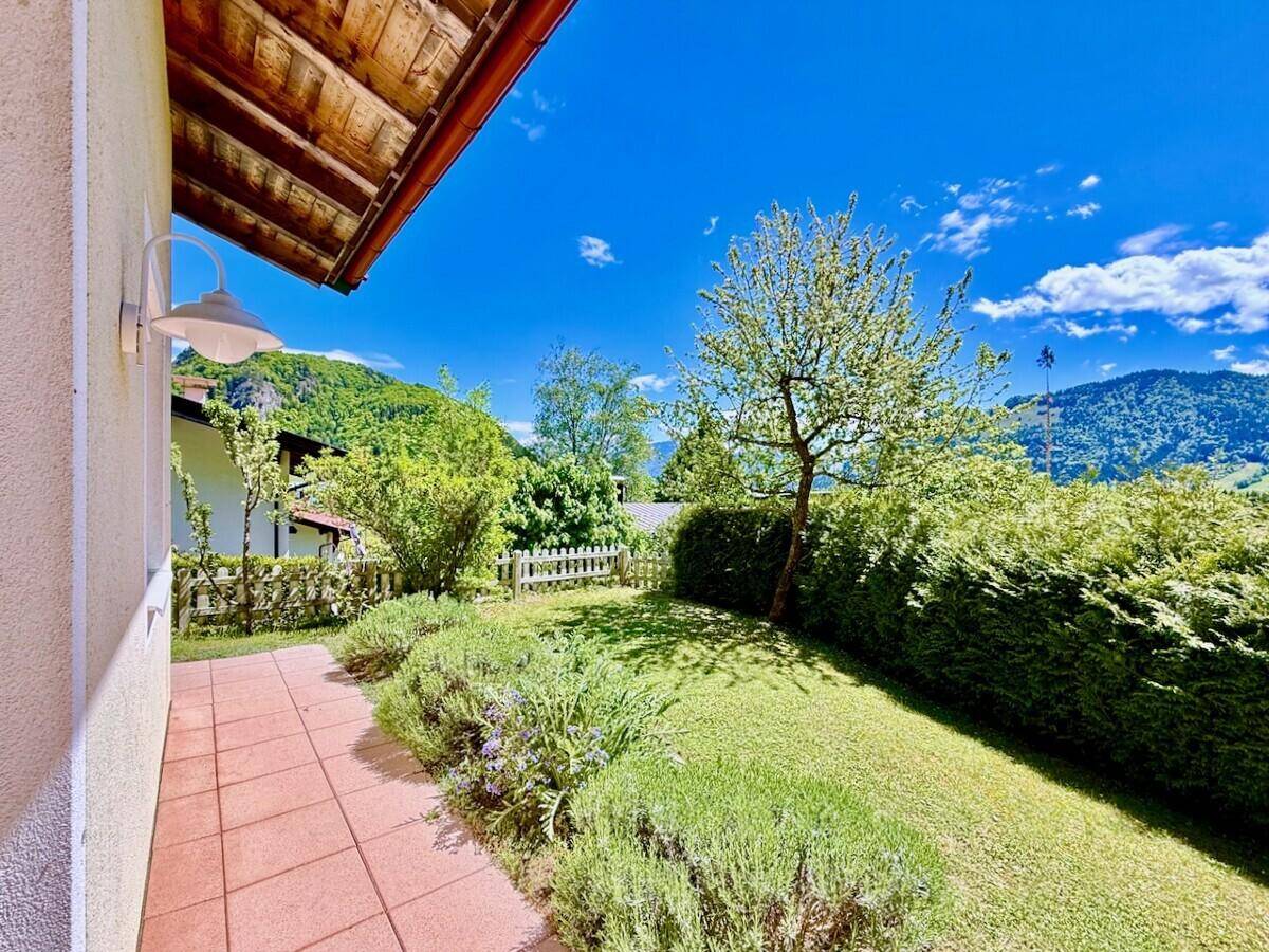 Gepflegter Gartenbereich mit Rasenfläche, Hecke und Bergblick.