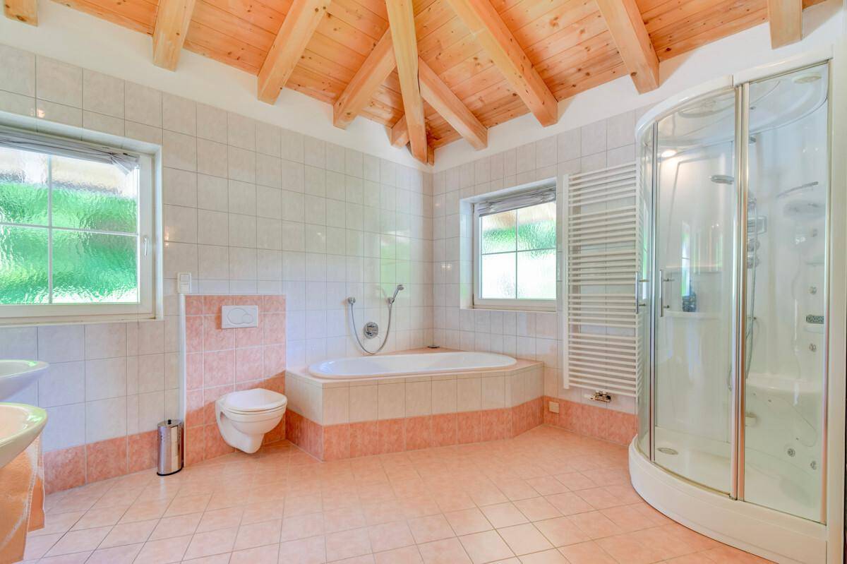Geräumiges Badezimmer mit Eckbadewanne, Duschkabine und Holzbalkendecke.
