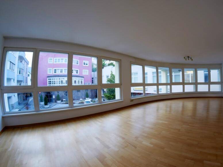 Geräumiges Wohnzimmer mit vielen Fenstern, hellem Laminatboden und Blick auf die Umgebung.
