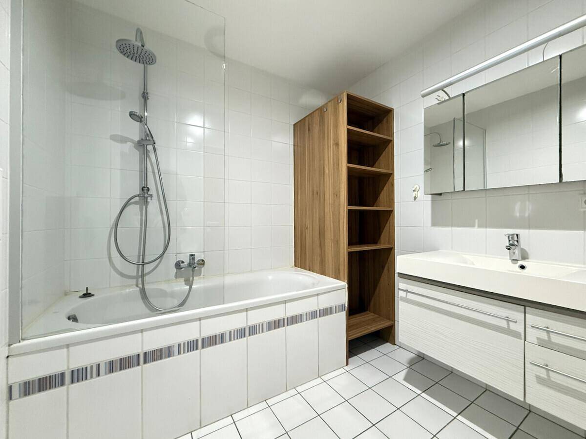 Helles Badezimmer mit Badewanne, Duschvorrichtung, Waschtisch und Holzregal.