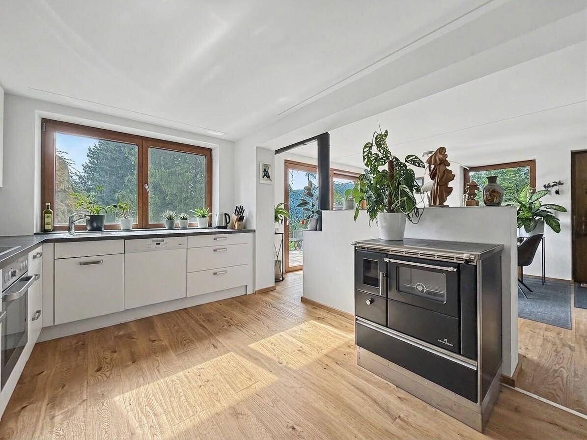 Helle Küche mit weißen Schränken, Holzboden und einem traditionellen schwarzen Holzofen.