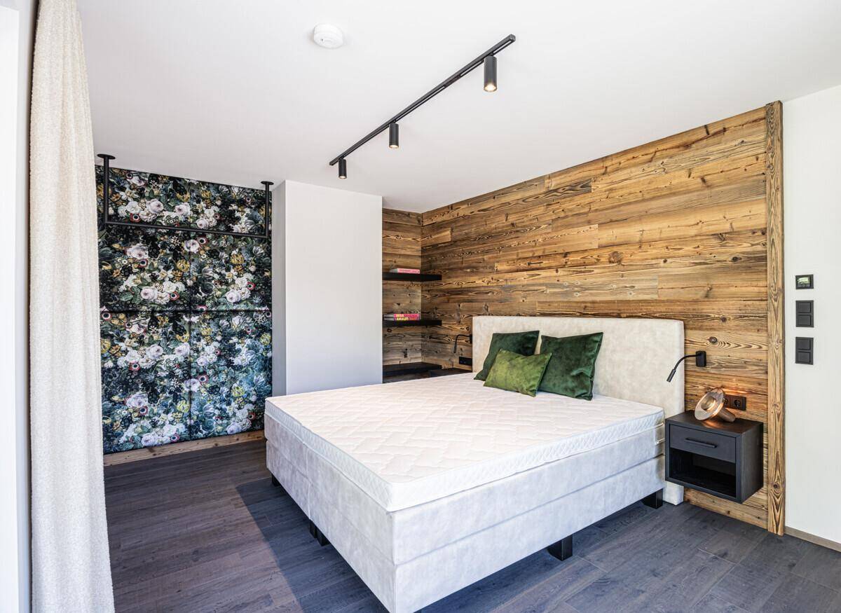 Schlafzimmer mit Holzakzentwand, floraler Tapete und modernem Bett für eine stilvolle Atmosphäre.