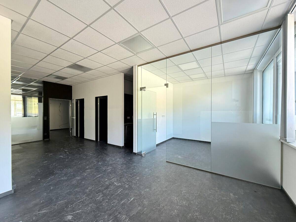 Offener Bürobereich mit modernen Glastrennwänden und dunklem Boden, bereit für die individuelle Gestaltung.