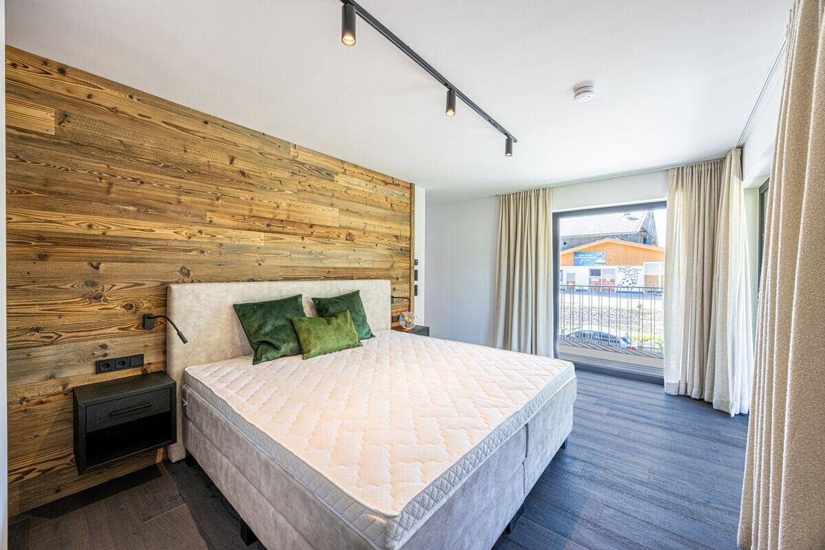 Gemütliches Schlafzimmer mit Holzwand, großem Bett und viel Tageslicht durch das Fenster.