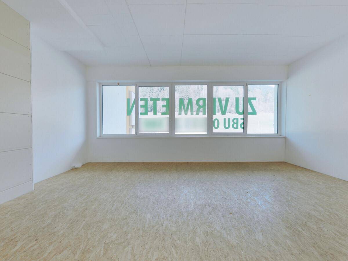 Großer, leerer Gewerberaum mit OSB-Boden und einer Reihe von Fenstern, die viel natürliches Licht bieten.
