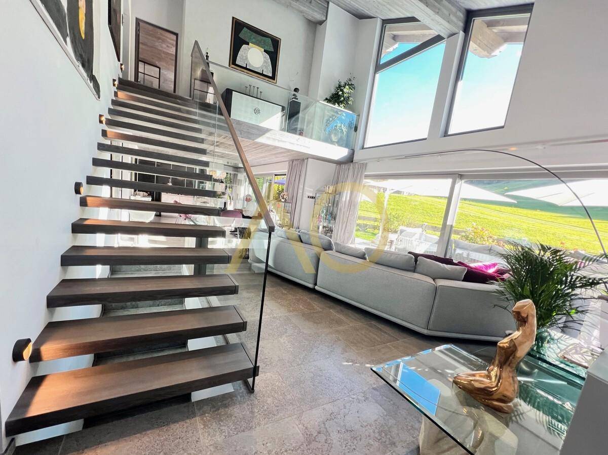 Offener Wohnbereich mit moderner Treppe, Glasgeländer und großen Fensterfronten.