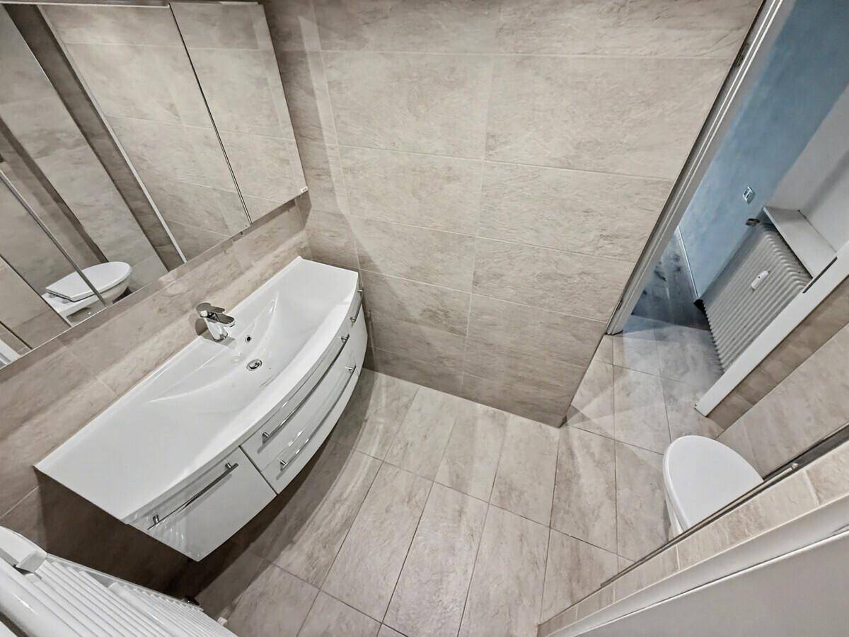 Helles Badezimmer mit modernem Waschtisch, Spiegelschrank und beigefarbenen Fliesen.