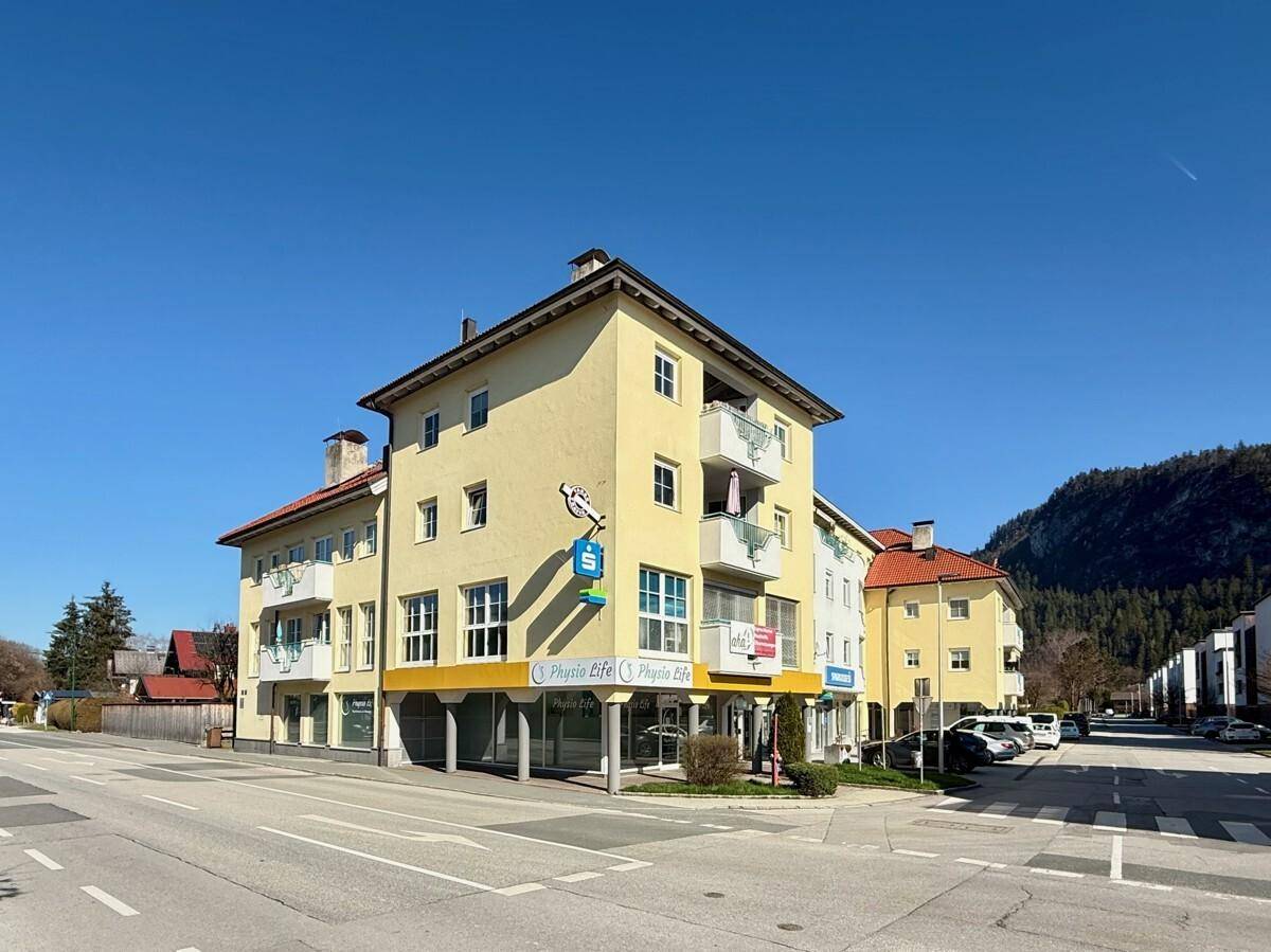 Gelbes Mehrfamilienhaus mit Geschäften im Erdgeschoss und Balkonen unter blauem Himmel.