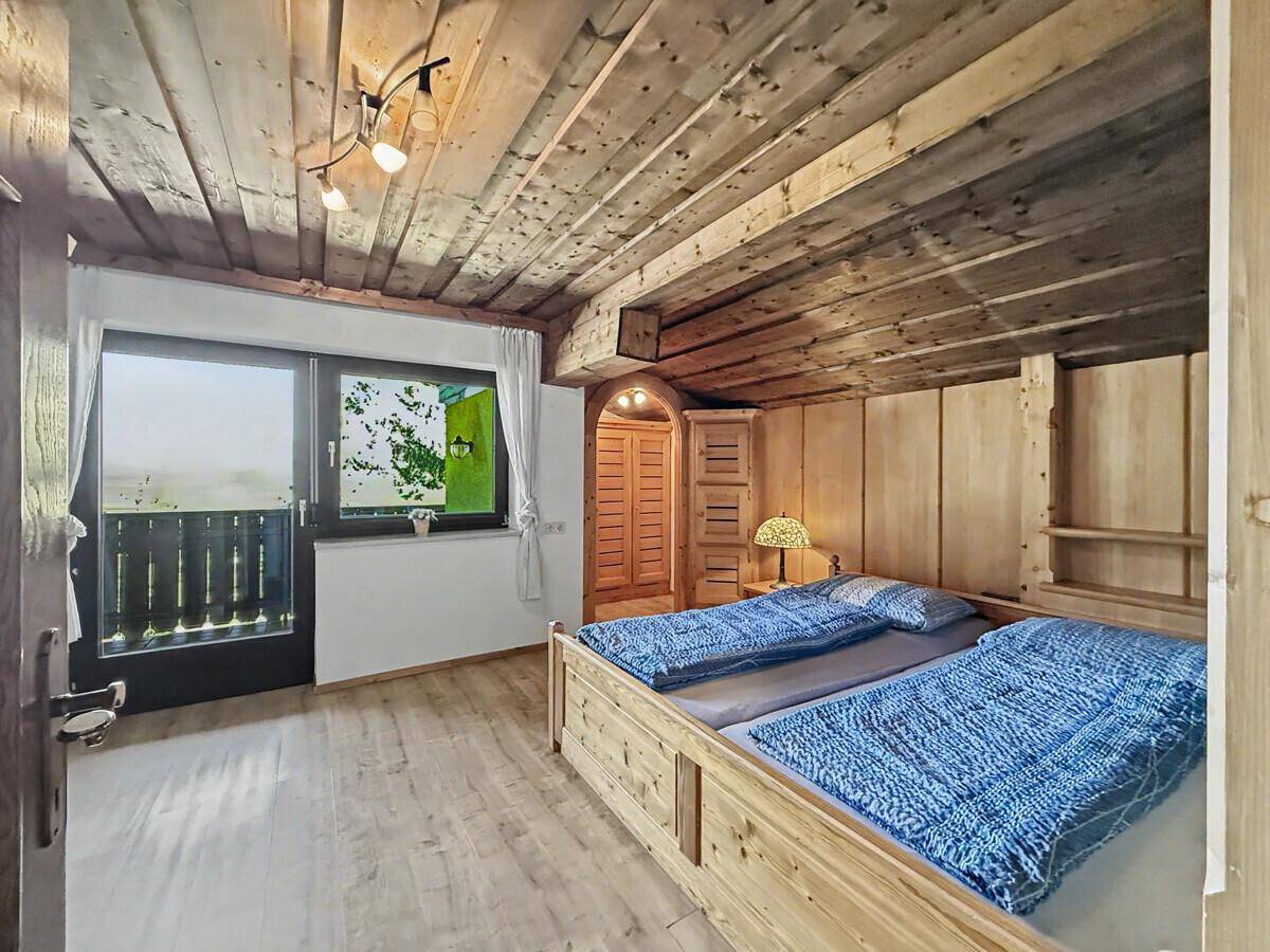 Rustikales Schlafzimmer mit Holzbalkendecke und Balkonzugang, bietet viel natürliches Licht.