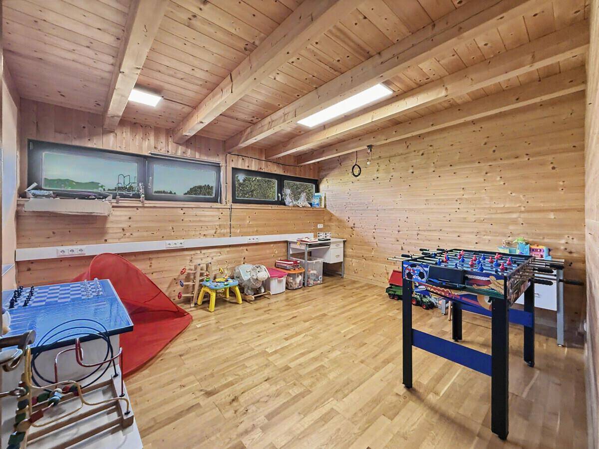 Geräumiges Spielzimmer mit Holzboden und -wänden, ausgestattet mit Tischfußball und Spielzeug.