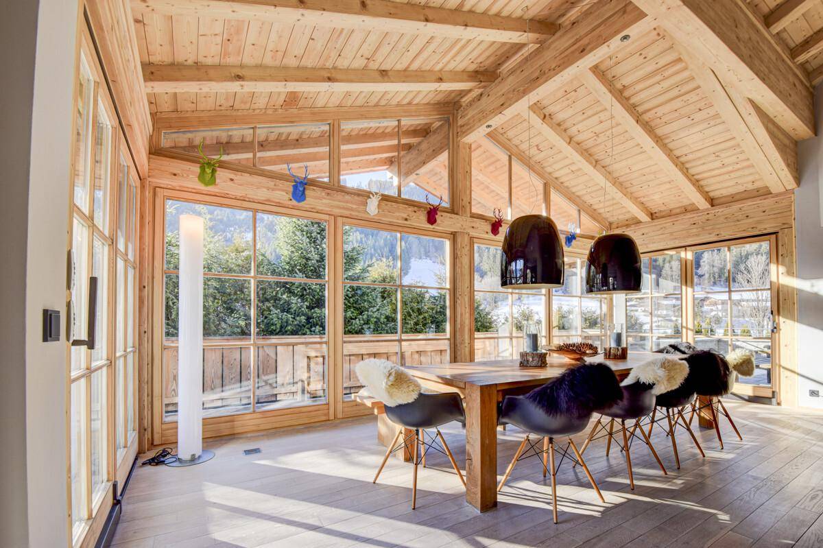 Heller Essbereich mit Holzbalkendecke, großen Fensterfronten und Blick auf die verschneite Landschaft.