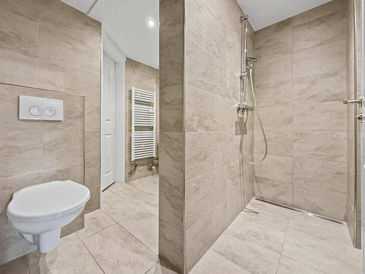 Modernes Badezimmer mit begehbarer Dusche, Wand-WC und beigefarbenen Fliesen.