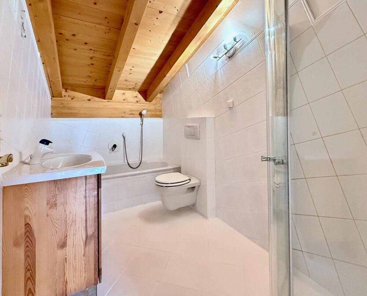 Helles Badezimmer mit Badewanne, Toilette, Waschbecken und Duschkabine unter Holzbalken.