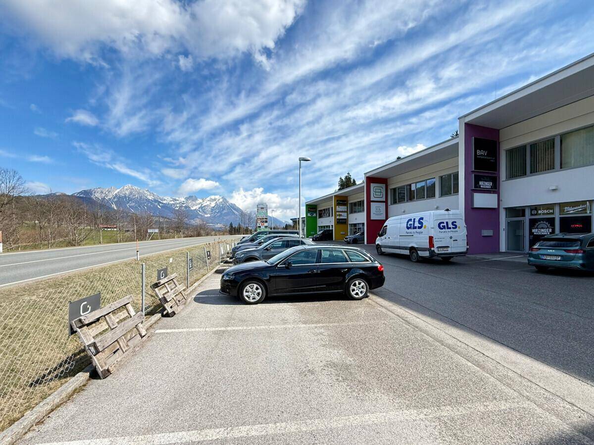 Modernes Geschäftsgebäude mit Parkplätzen und Blick auf schneebedeckte Berge unter blauem Himmel.