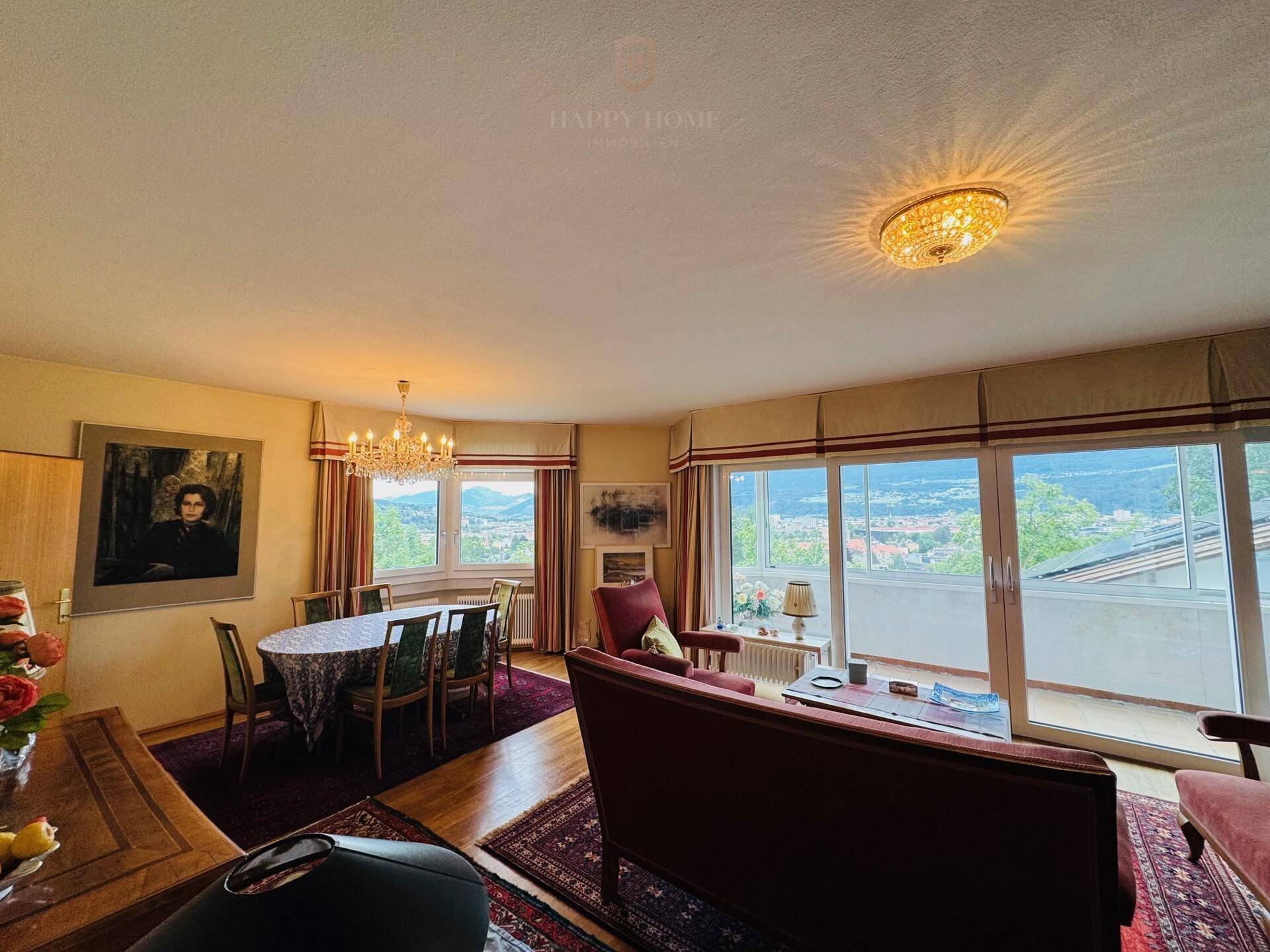Geräumiger Wohn- und Essbereich mit Holzboden, großen Fenstern und Zugang zu einem Balkon mit Weitblick.
