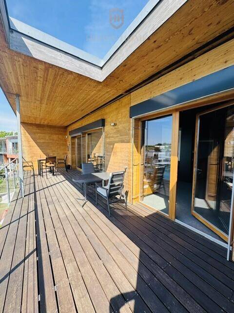 Geräumige Holzterrasse mit Sitzgelegenheiten und weitem Blick auf den See unter blauem Himmel.