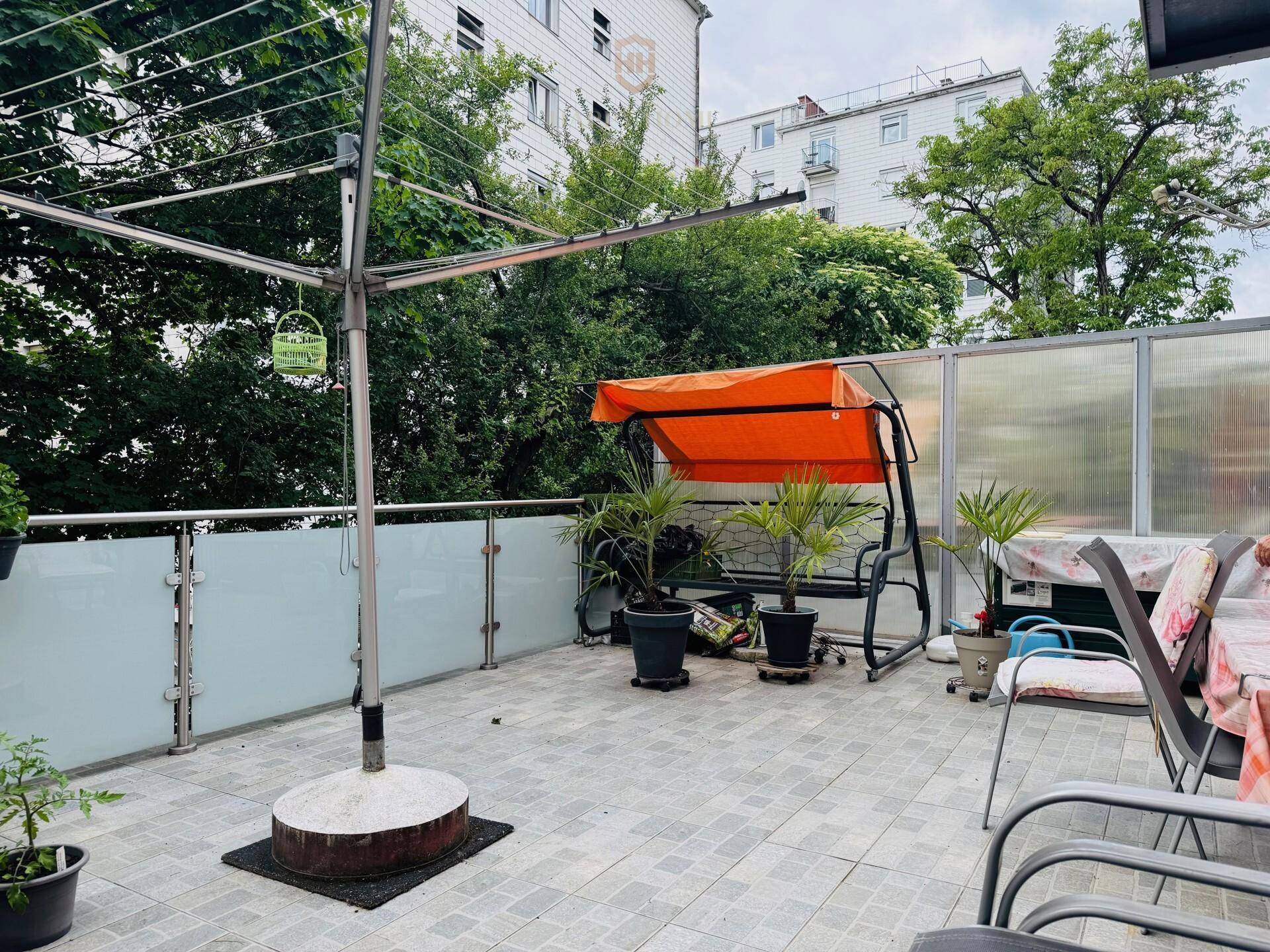 Große geflieste Terrasse mit Sitzgelegenheiten, Pflanzen und Wäscheständer, umgeben von Bäumen.