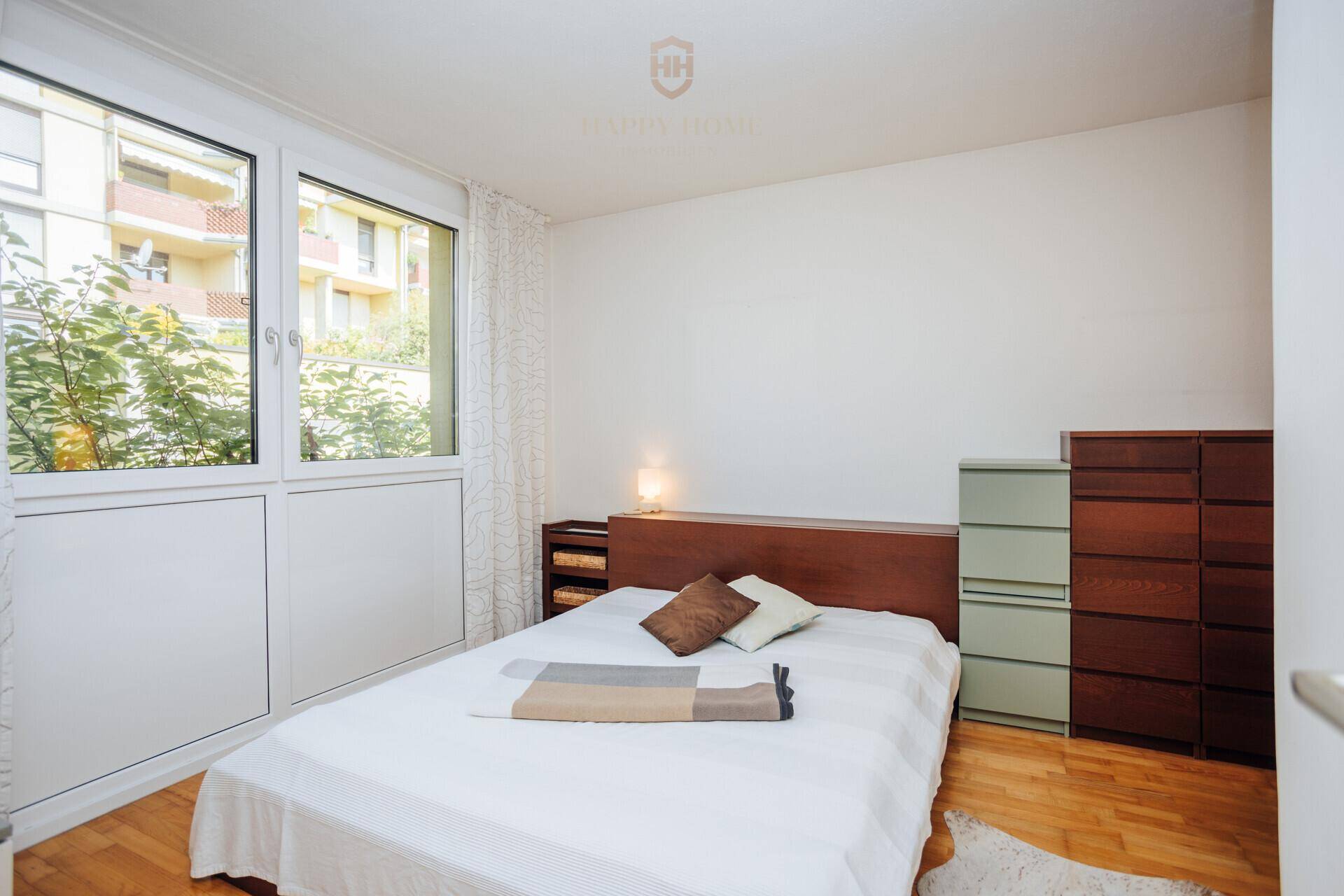 Helles Schlafzimmer mit großen Fenstern, Holzboden und Blick ins Grüne.