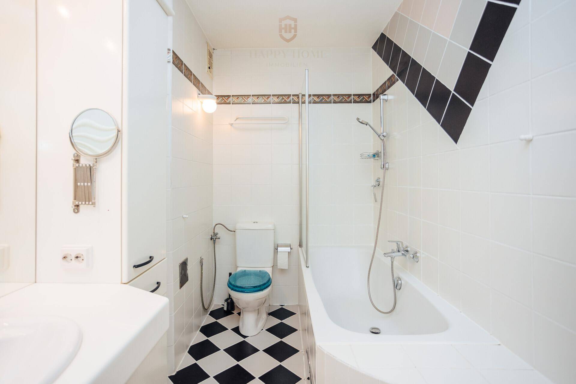 Badezimmer mit Badewanne, integrierter Dusche und WC, sowie schwarz-weißem Fliesenboden.