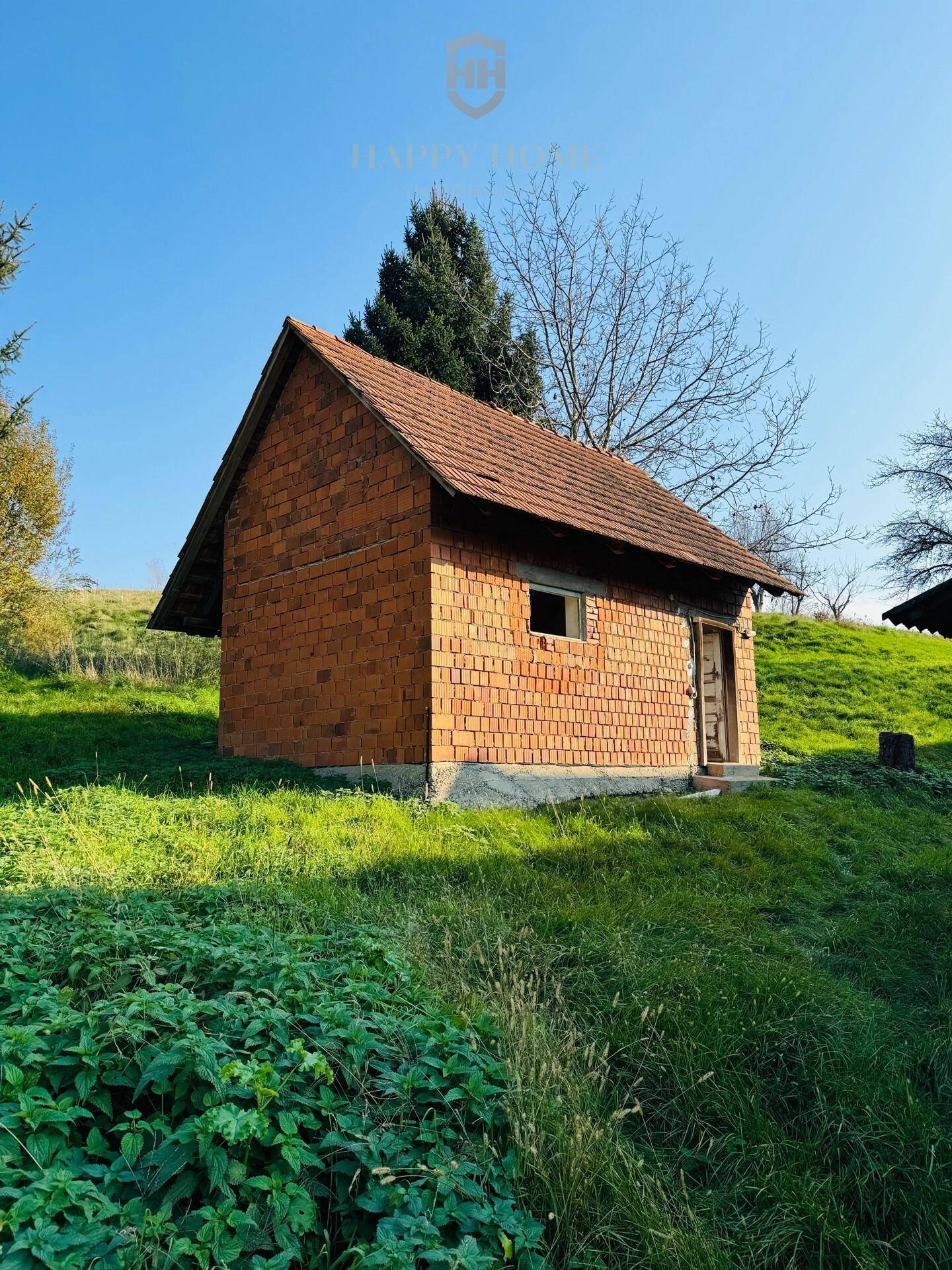 Kleines, freistehendes Ziegelgebäude mit Ziegeldach auf einem sonnigen, grünen Hügel.