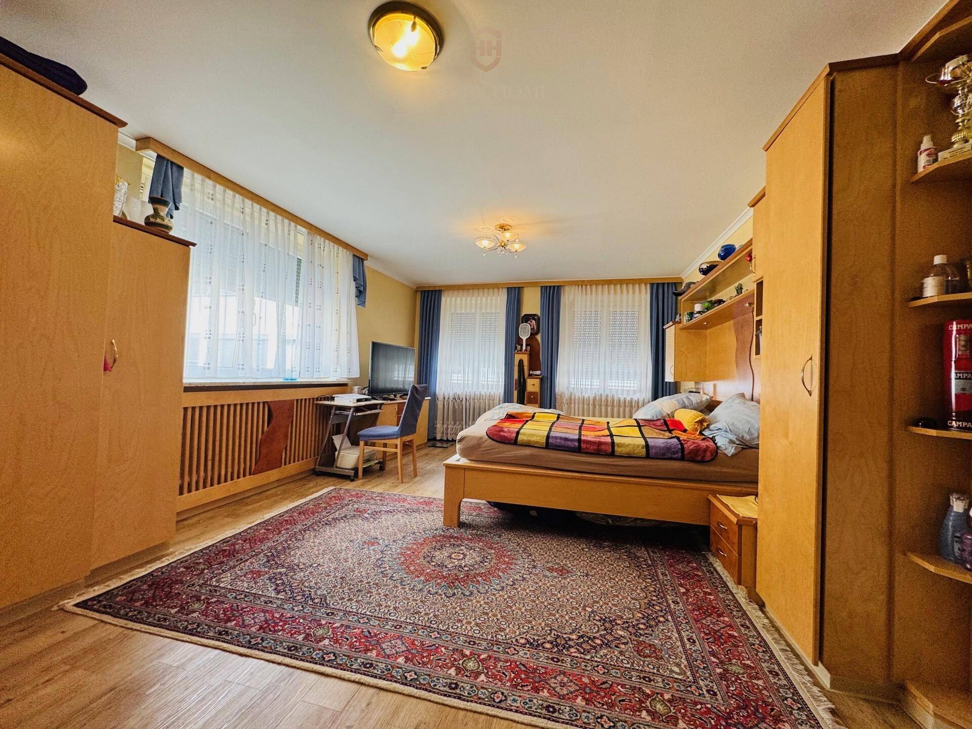 Geräumiges Schlafzimmer mit Holzmöbeln, Teppich und Fenstern mit blauen Vorhängen.