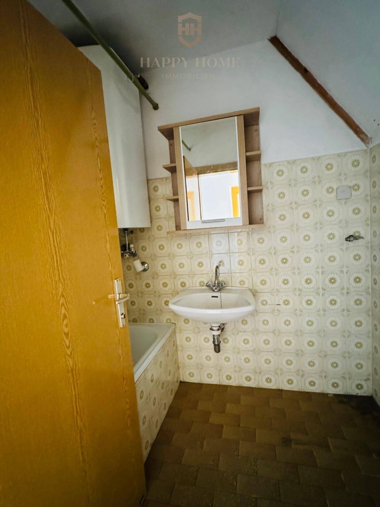 Veraltetes Badezimmer mit gemusterten Fliesen, Waschbecken und Badewanne, renovierungsbedürftig.