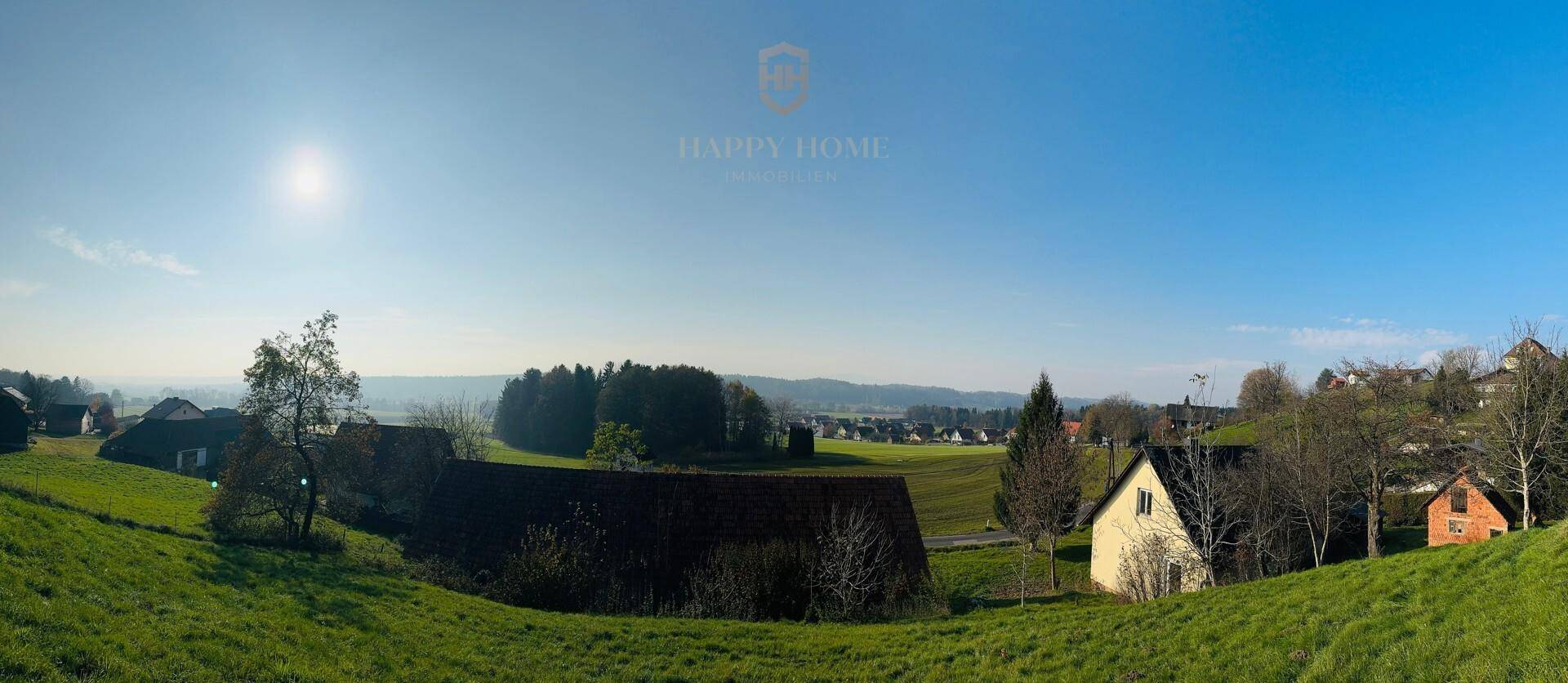 Weitläufiger Panoramablick über die grüne Hügellandschaft mit vereinzelten Häusern und Wald.