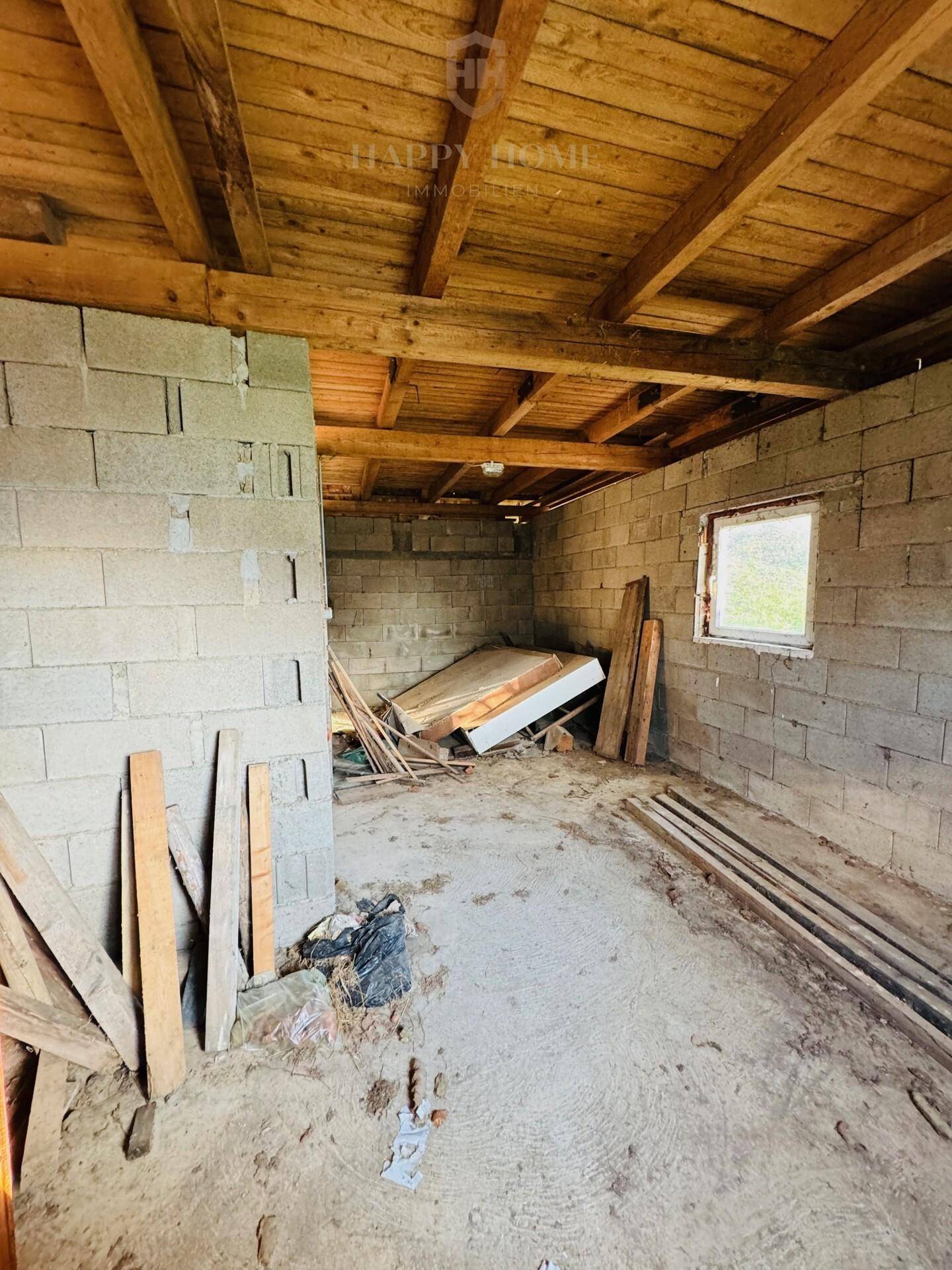 Leerer Lagerraum im Nebengebäude mit Betonwänden und Holzdach, renovierungsbedürftig.