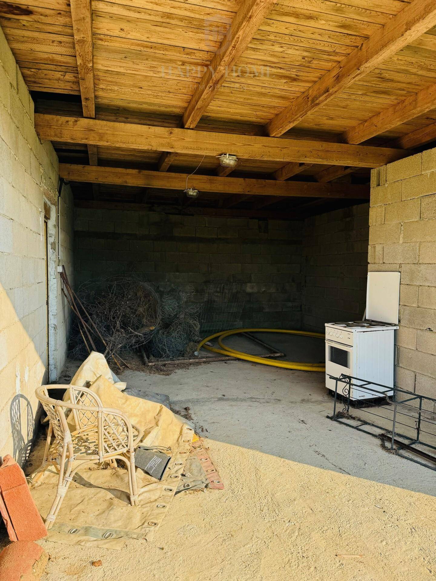 Überdachter Außenbereich oder Schuppen mit Betonwänden und Holzdach, als Lager genutzt.