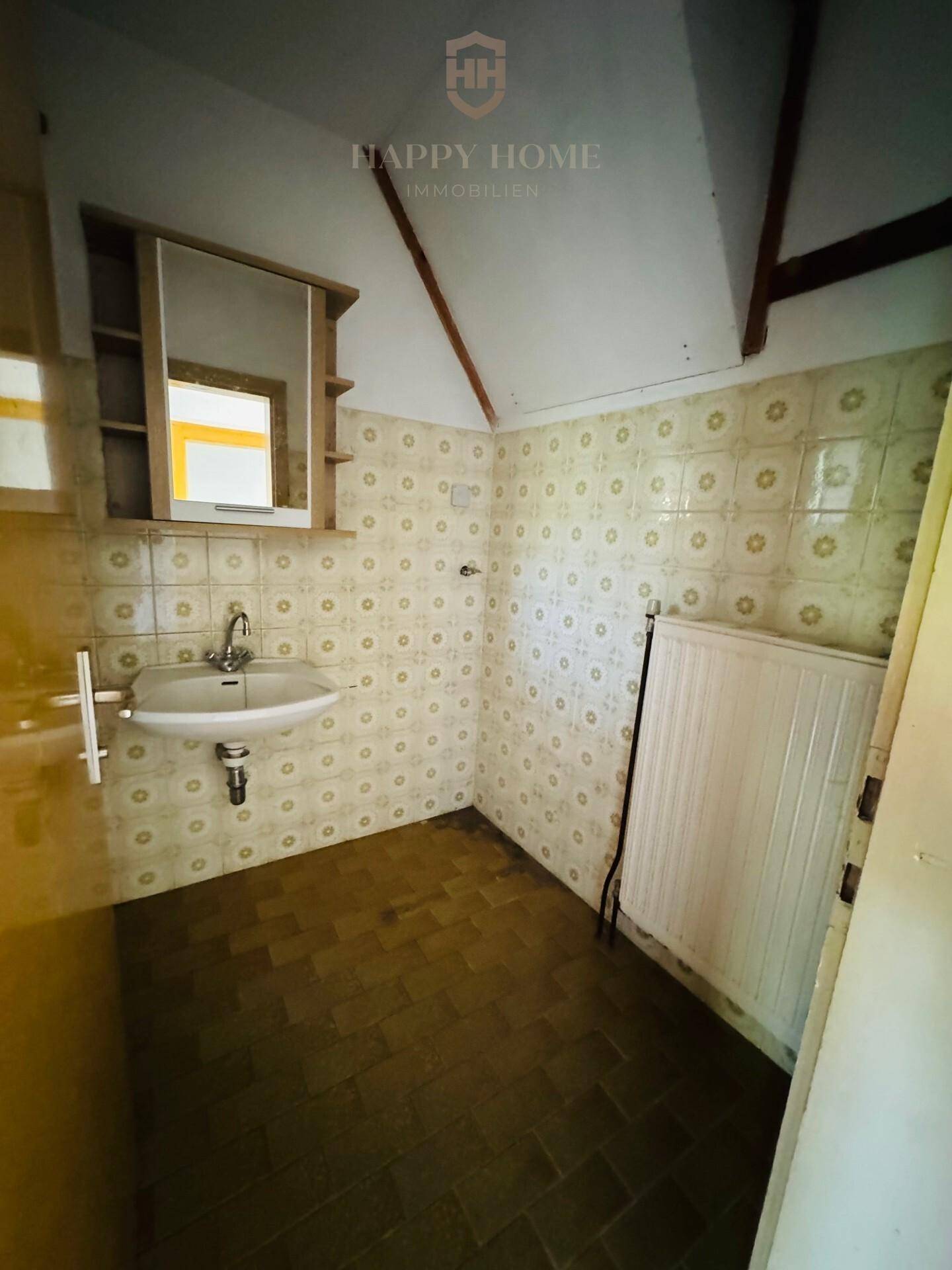 Veraltetes Badezimmer mit gemusterten Fliesen, Waschbecken und Badewanne, renovierungsbedürftig.