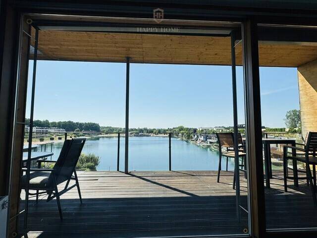 Heller Innenraum mit großen Schiebetüren, die sich zu einer Holzterrasse mit Seeblick öffnen.