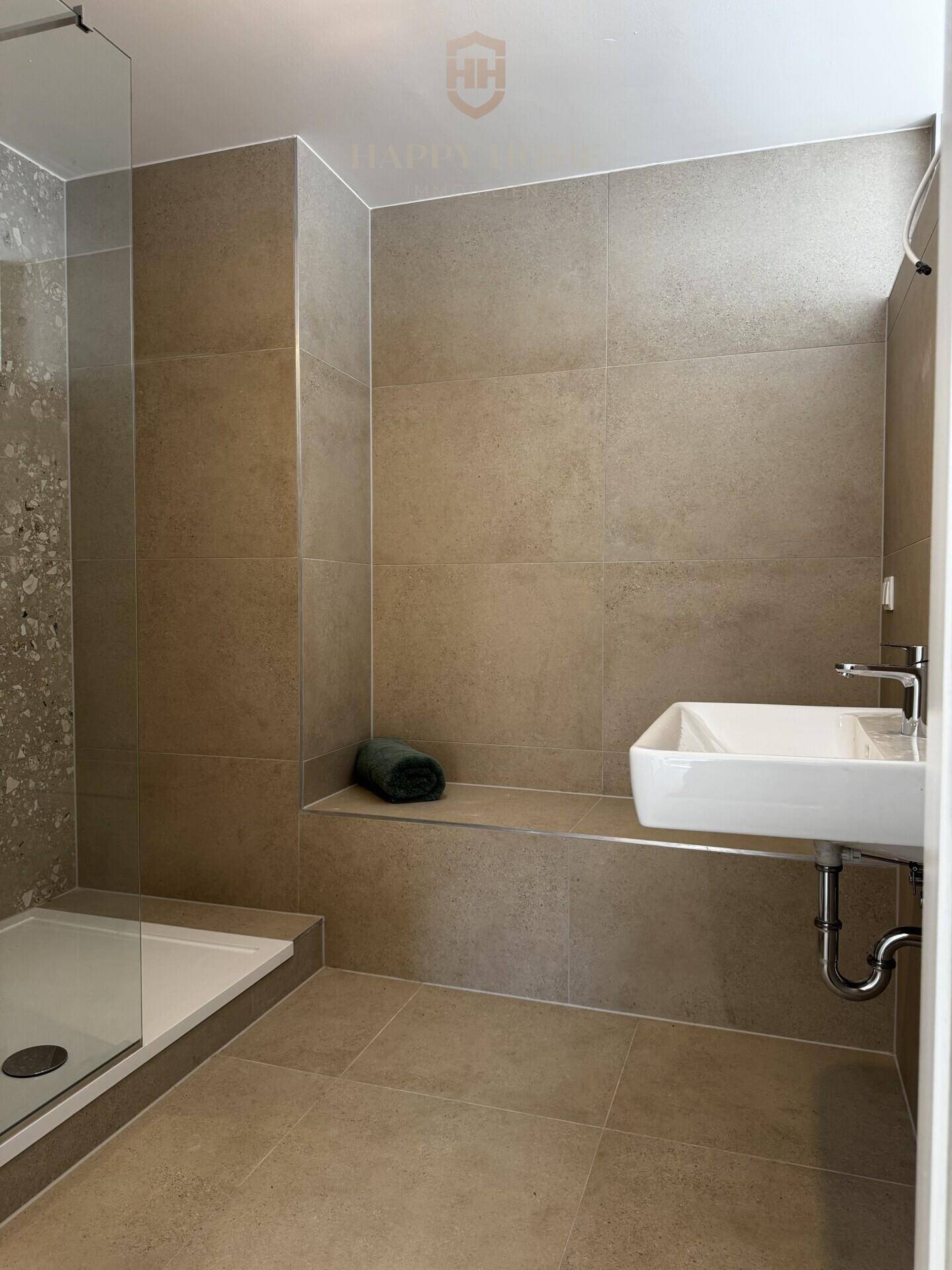 Modernes Badezimmer mit begehbarer Dusche, Wandwaschbecken und großen beigefarbenen Fliesen.