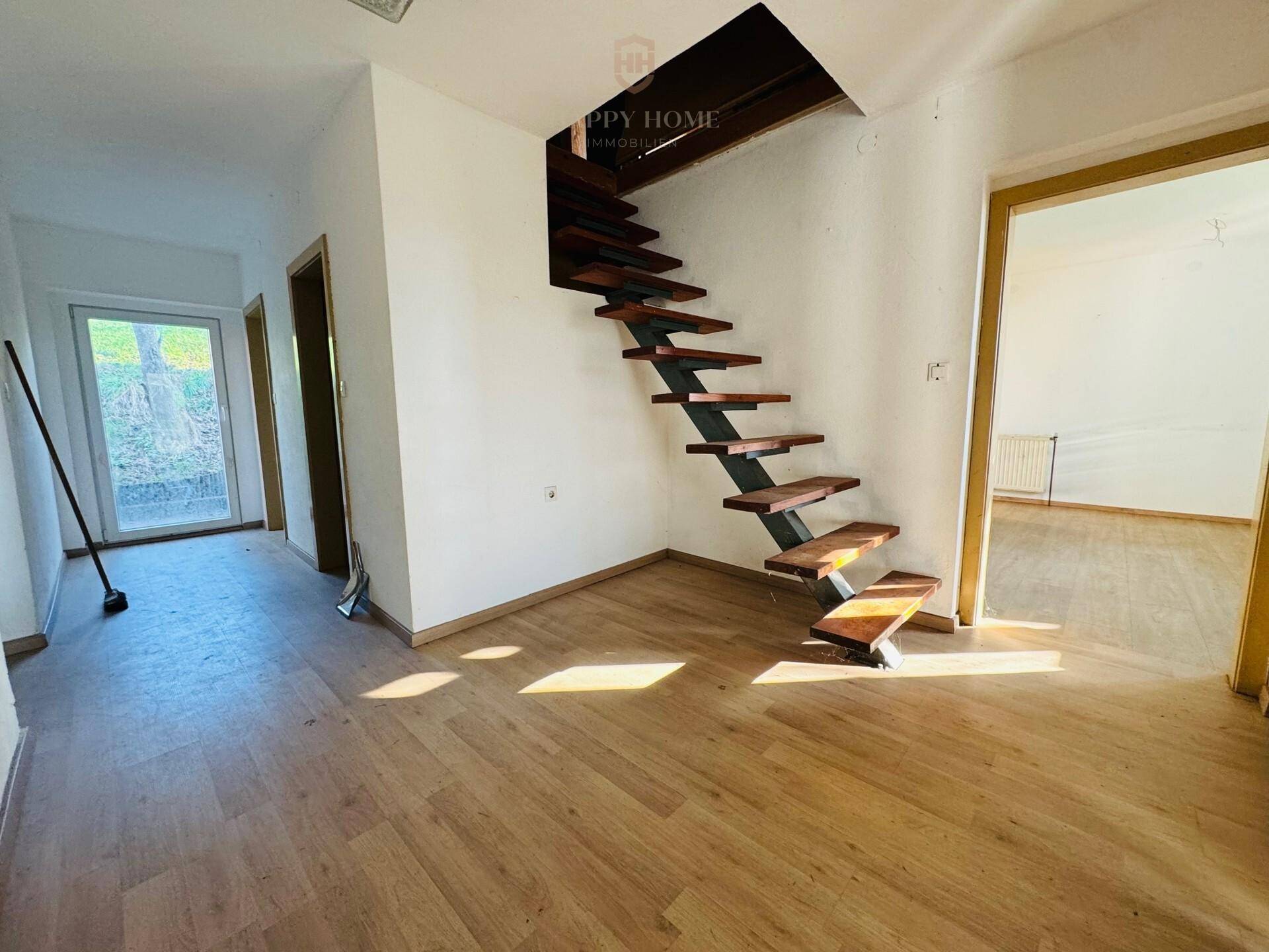Heller Eingangsbereich mit Holztreppe und Laminatboden, führt zu weiteren Räumen.