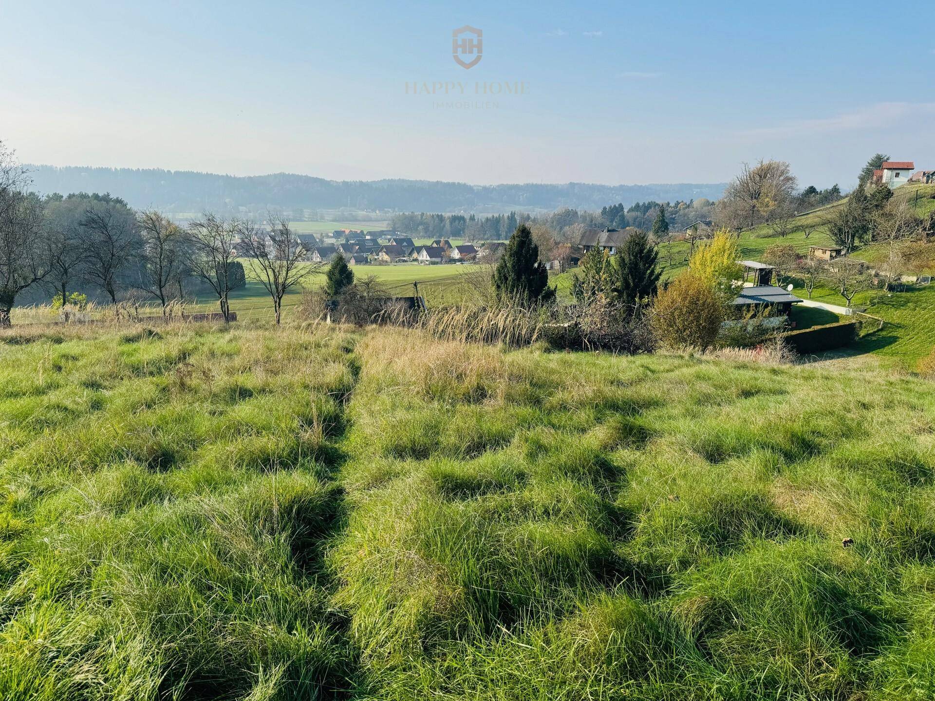 Grüne Wiesenfläche mit Blick auf die umliegende ländliche Bebauung und Hügel.
