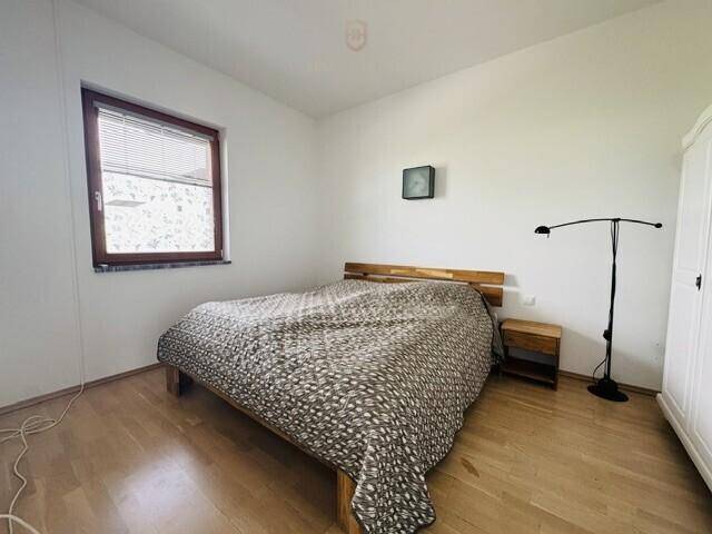 Schlafzimmer mit Holzbett und Parkettboden, ausgestattet mit einem Fenster und Jalousien.