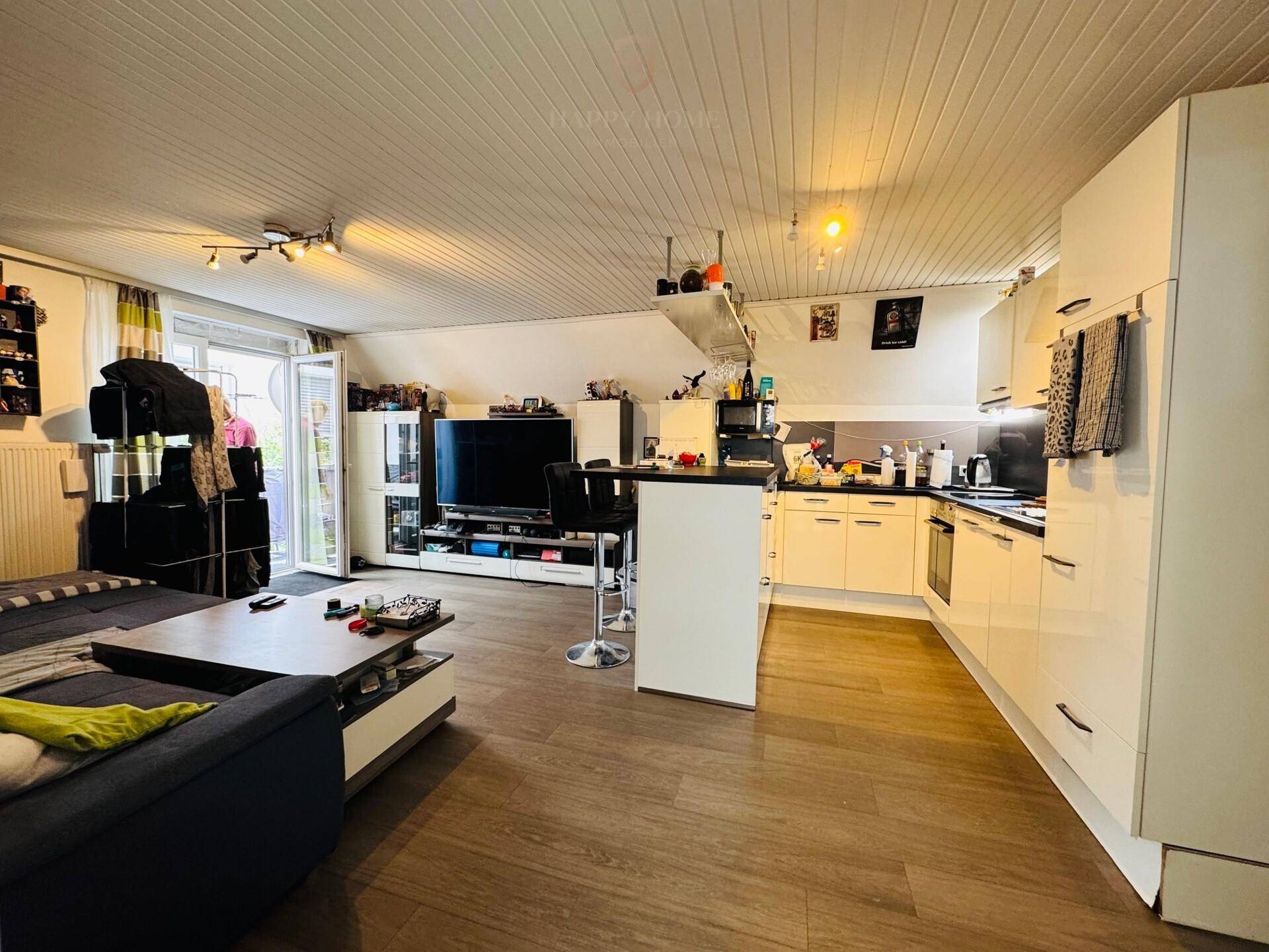 Offener Wohnbereich mit integrierter Küche, Sofa, Fernseher und Zugang zu einem Balkon.