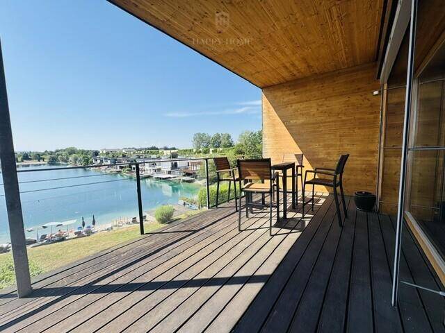 Sonniger Terrassenbereich mit Holzboden und Möbeln, der einen malerischen Blick auf den See bietet.