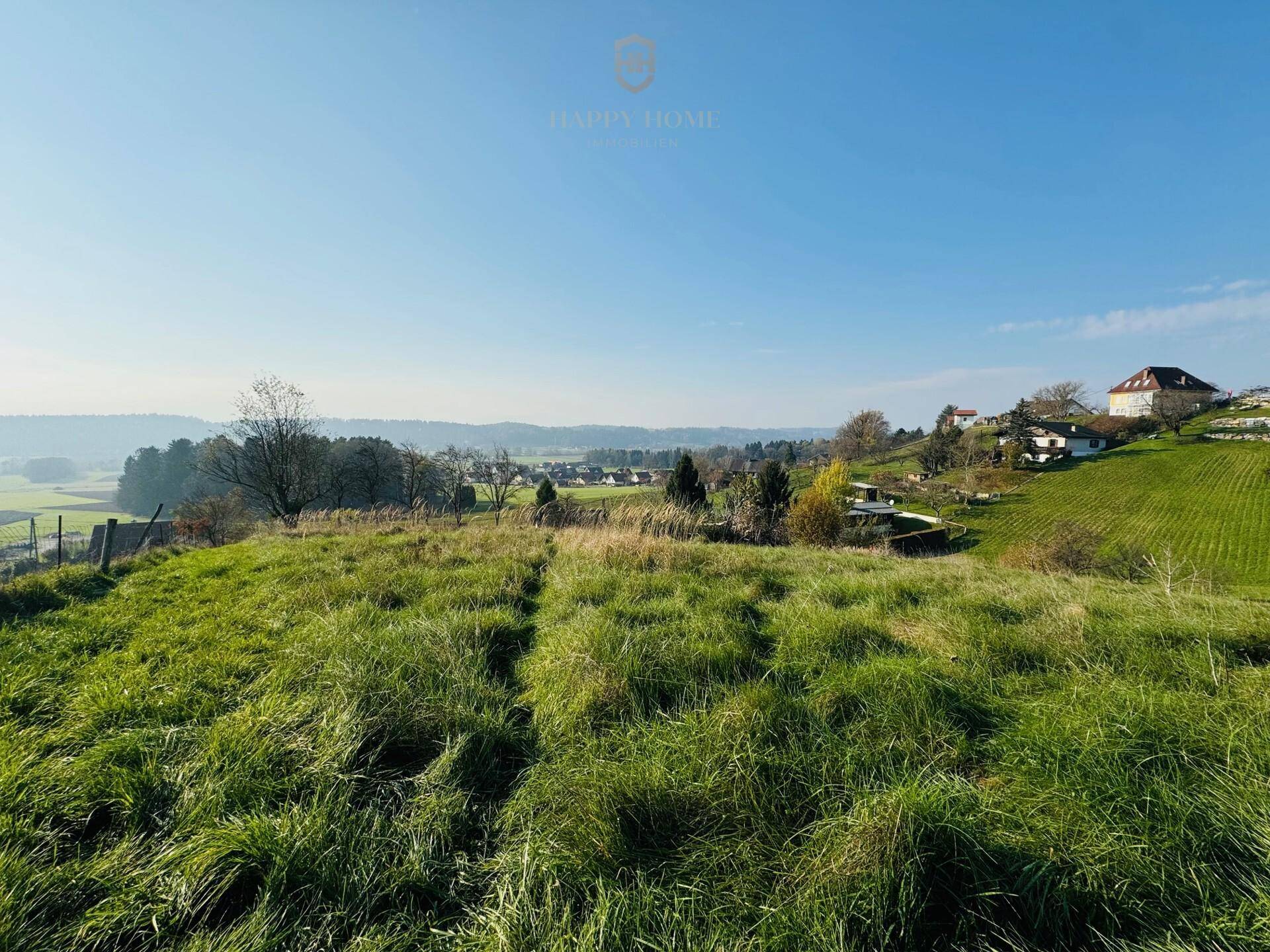 Grüne Wiesenfläche mit Blick auf die umliegende ländliche Bebauung und Hügel.