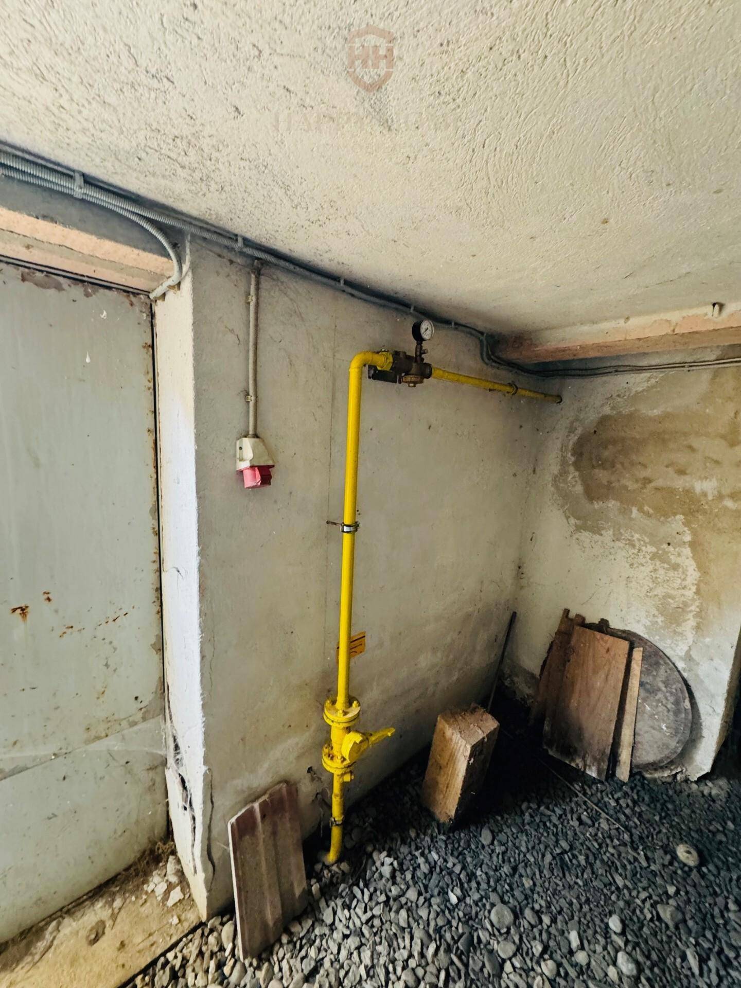 Kellerbereich mit sichtbaren Gasleitungen und einfacher Elektroinstallation, in Rohbauzustand.