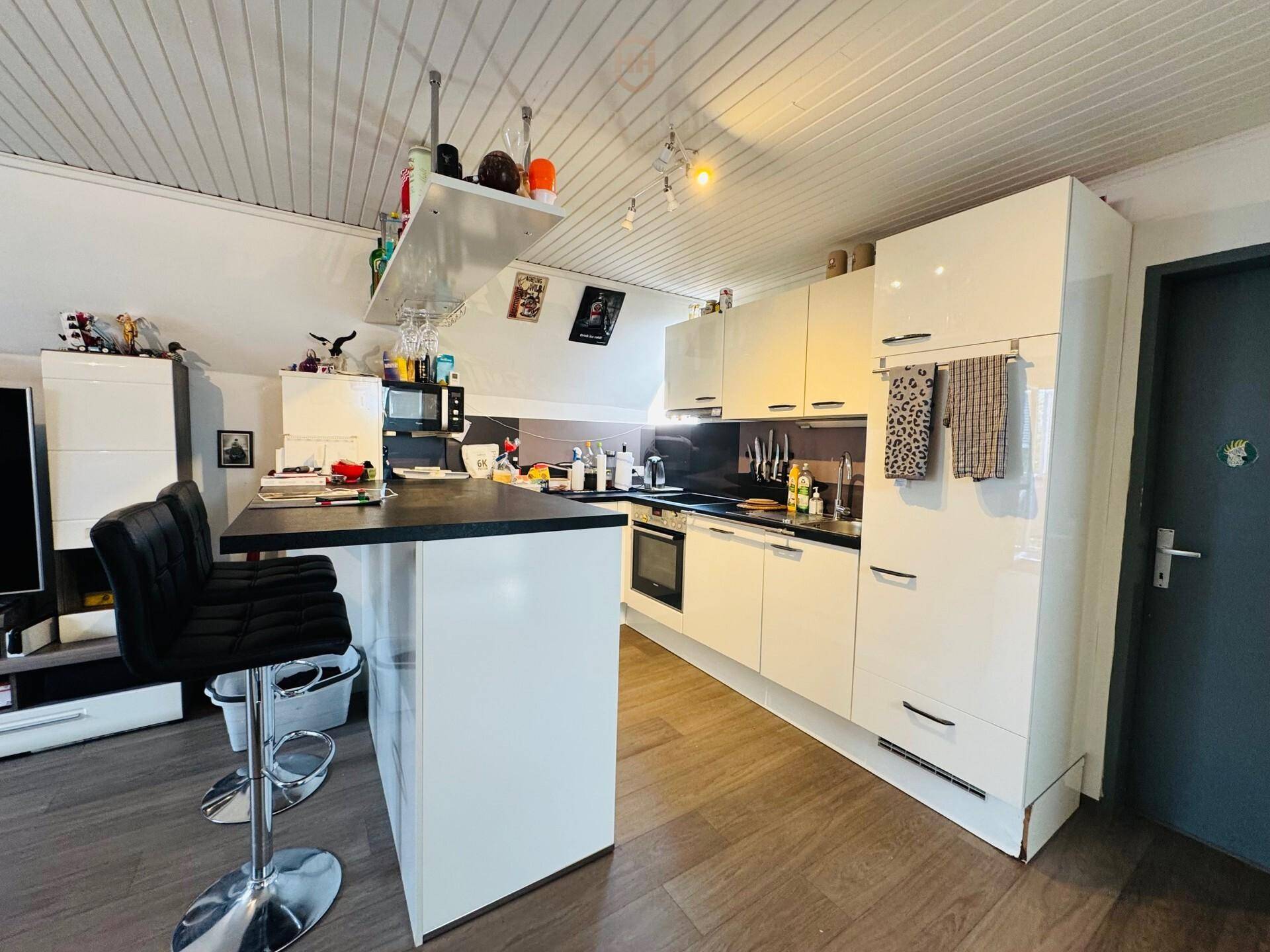 Moderne Küche mit weißen Hochglanzschränken, Frühstücksbar und Holzdeckenverkleidung.