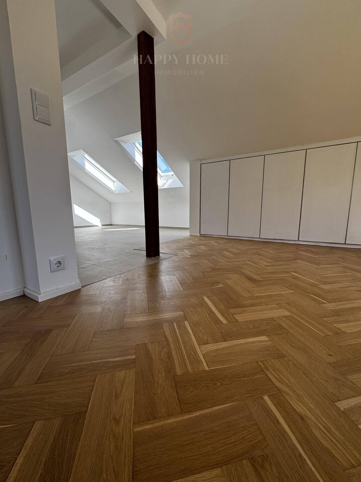 Offener Dachgeschossbereich mit Fischgrätparkett, Dachfenstern und eingebauten Schränken.