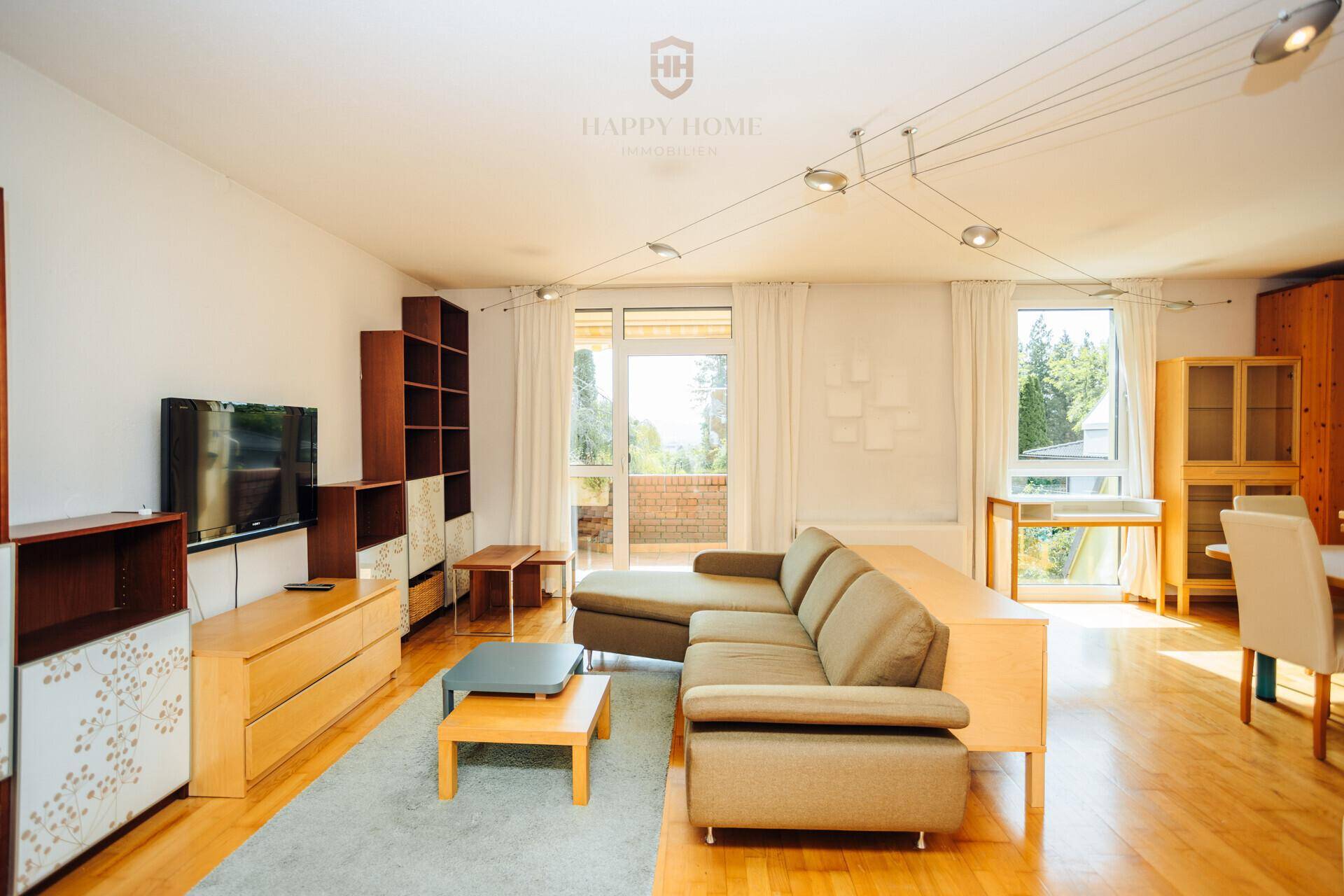 Geräumiges Wohnzimmer mit Holzfußboden, großen Fenstern und Zugang zu einem Balkon.